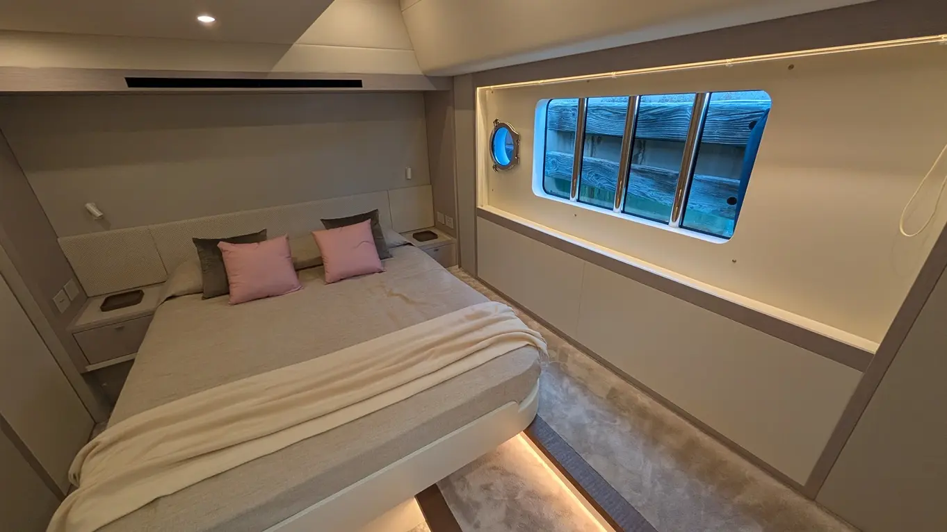 Modern bedroom with a double bed, light grey decor, pink cushions, and a circular blue window overlooking wooden panels.